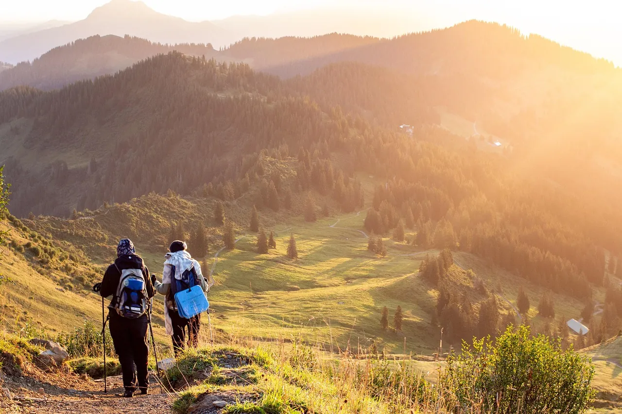 Hai người đi bộ đường núi dùng gậy trekking trên đường mòn lúc hoàng hôn